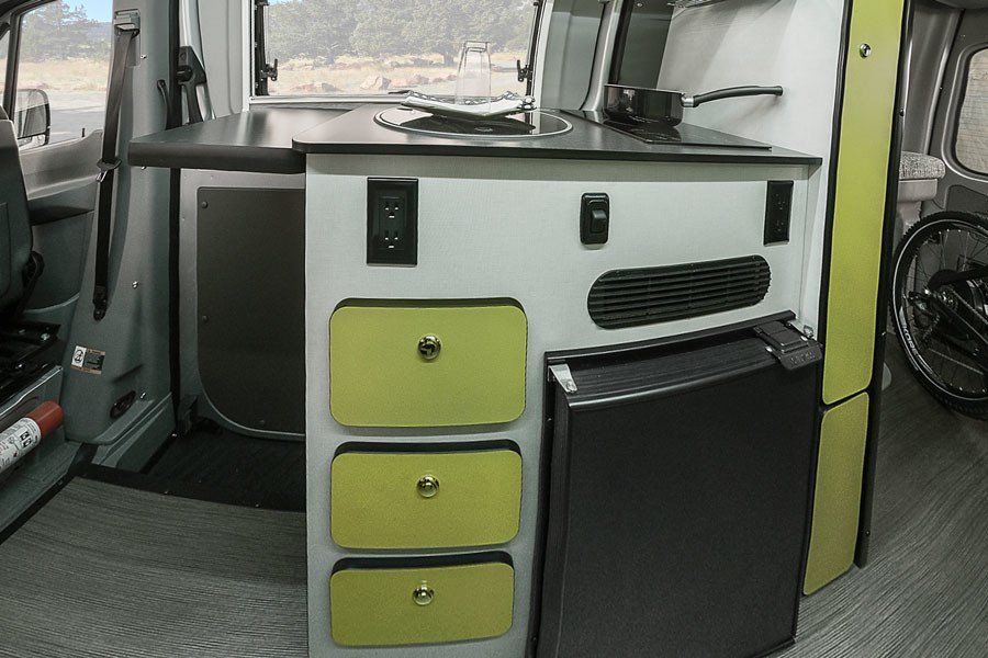 Compact RV rental interior featuring a kitchenette, lime green drawers, and a built-in fridge, perfect for mobile adventures.