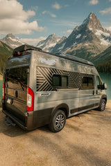 Grey rv rental with geometric decals, parked by a stunning lake & snow-capped mountains. Ideal for an outdoor adventure.