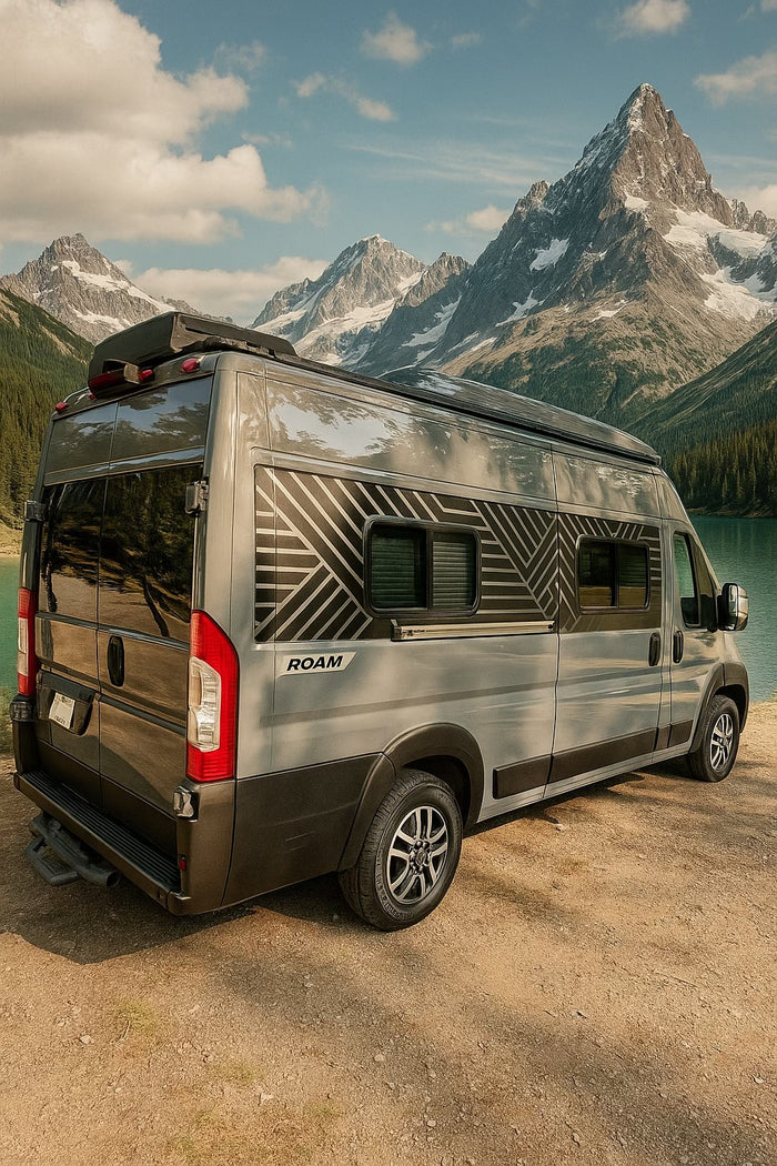Grey rv rental with geometric decals, parked by a stunning lake & snow-capped mountains. Ideal for an outdoor adventure.