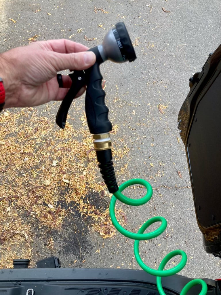 A hand holds a hose nozzle and coiled green hose, essentials for any RV rental adventure.