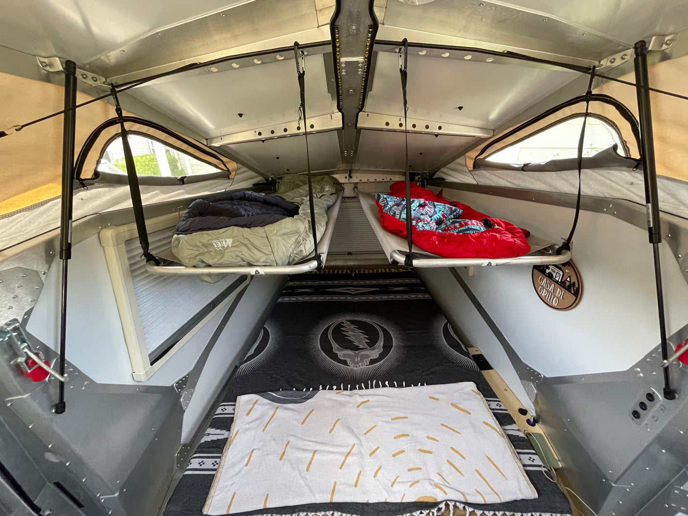 An RV rental interior reveals two suspended bunks with sleeping bags, and a Grateful Dead blanket below.