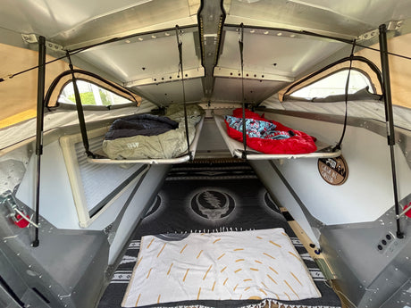 An RV rental interior reveals two suspended bunks with sleeping bags, and a Grateful Dead blanket below.