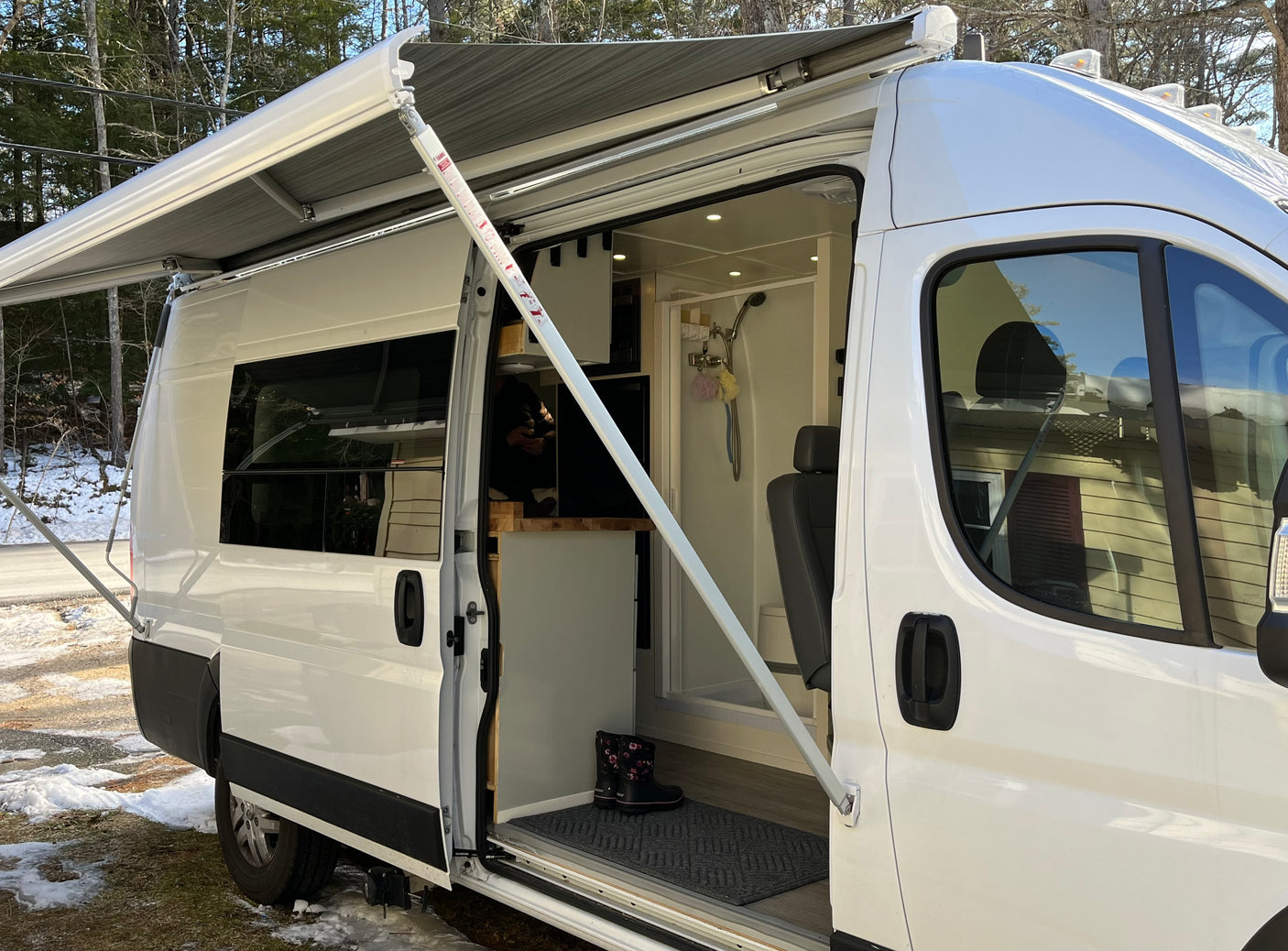 Open white rv rental showcasing interior kitchen, shower, and seating, with an extended awning and snowy ground.