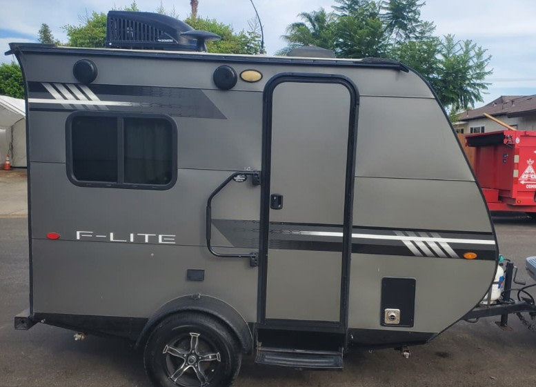  featuring a compact design and rooftop AC unit.|Silver Land Rover SUV towing a gray F-LITE travel trailer — photo 2
