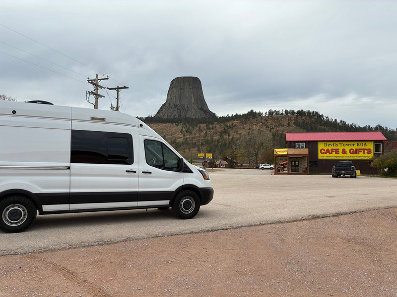 White RV rental van parked at Devils Tower KOA Cafe & Gifts with Devils Tower in the background under an overcast sky. — photo 13