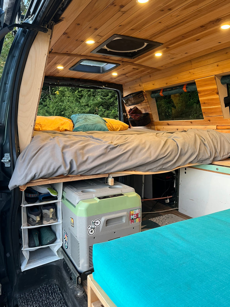 View of a modern RV rental interior featuring a cozy raised bed, wood-paneled ceiling, fridge, and built-in storage. — photo 3