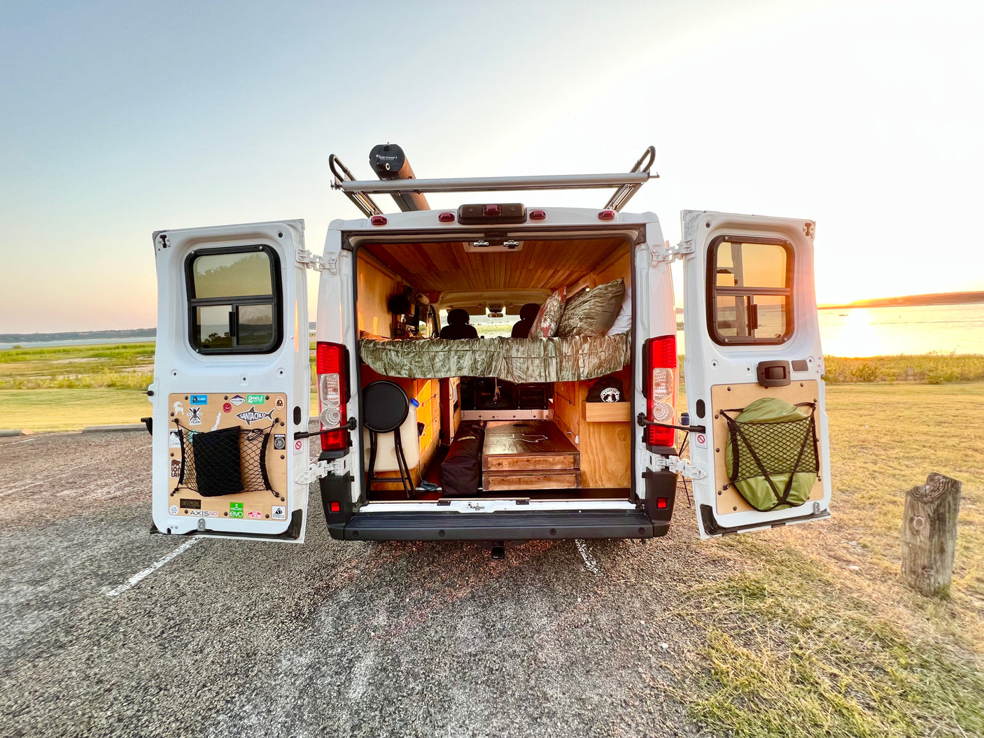 RV rental for adventure! Open doors show a custom camper interior, rooftop Road Shower, and sunset over the lake.