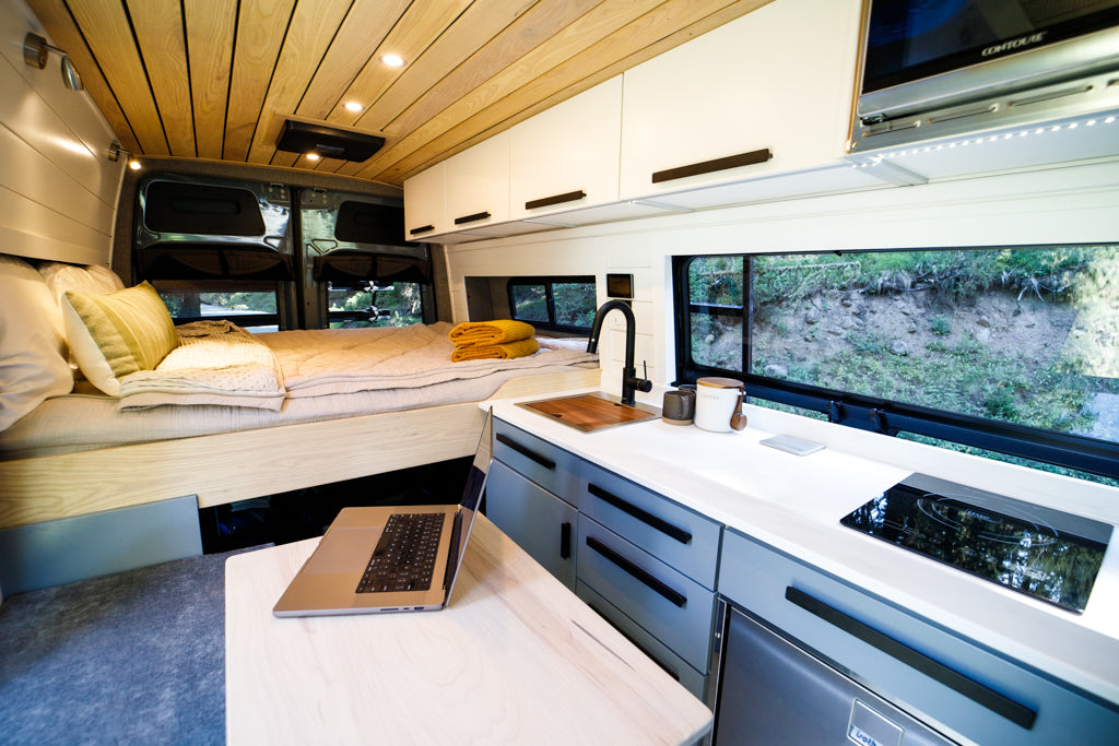 Luxurious RV rental interior with a cozy bed, full kitchen including a cooktop, and a laptop-ready workspace. Ideal for mobile living.