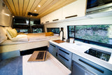 Luxurious RV rental interior with a cozy bed, full kitchen including a cooktop, and a laptop-ready workspace. Ideal for mobile living.