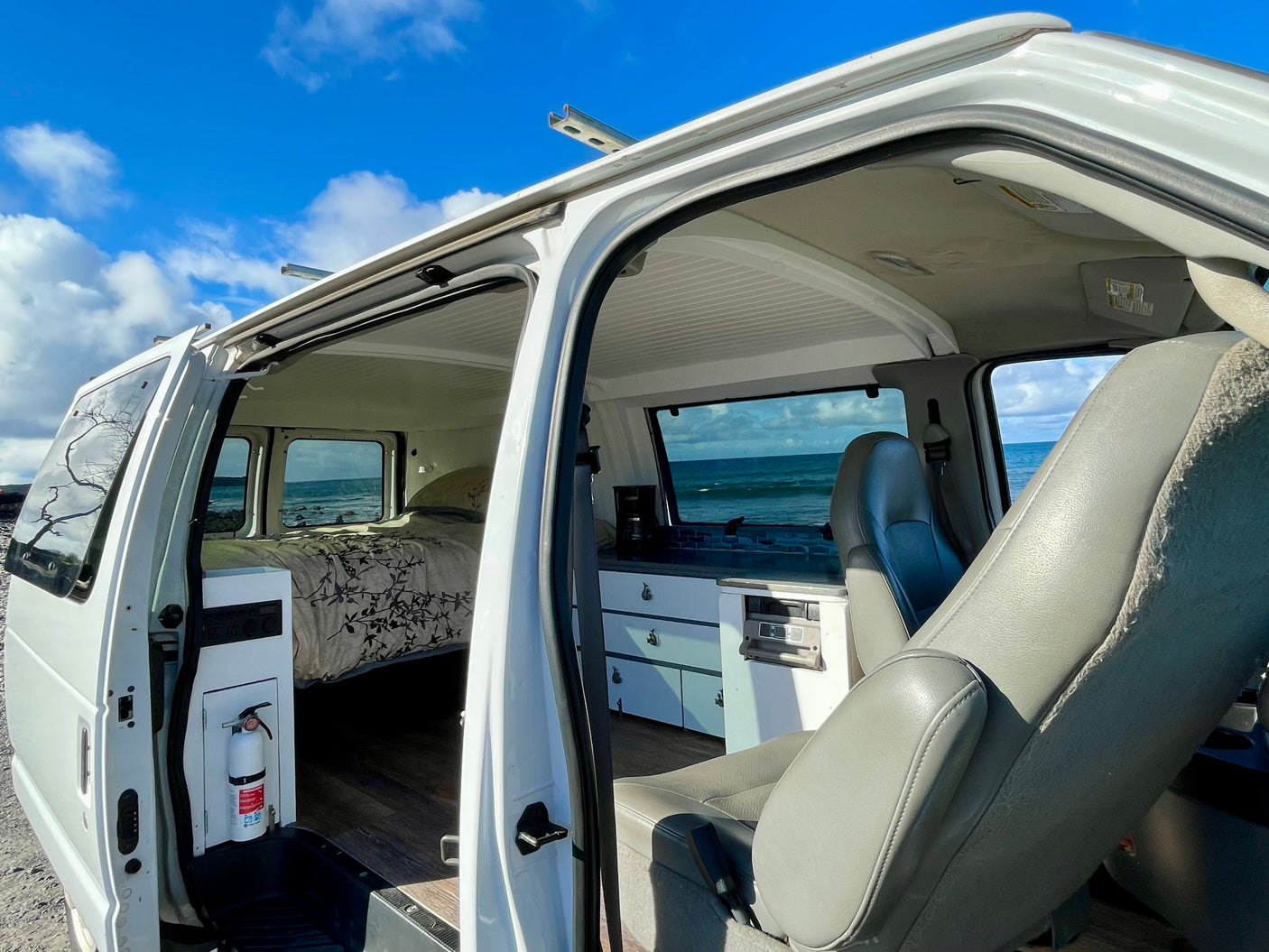 Explore the spacious interior of this RV rental, featuring a cozy bed and kitchen, with stunning ocean views.