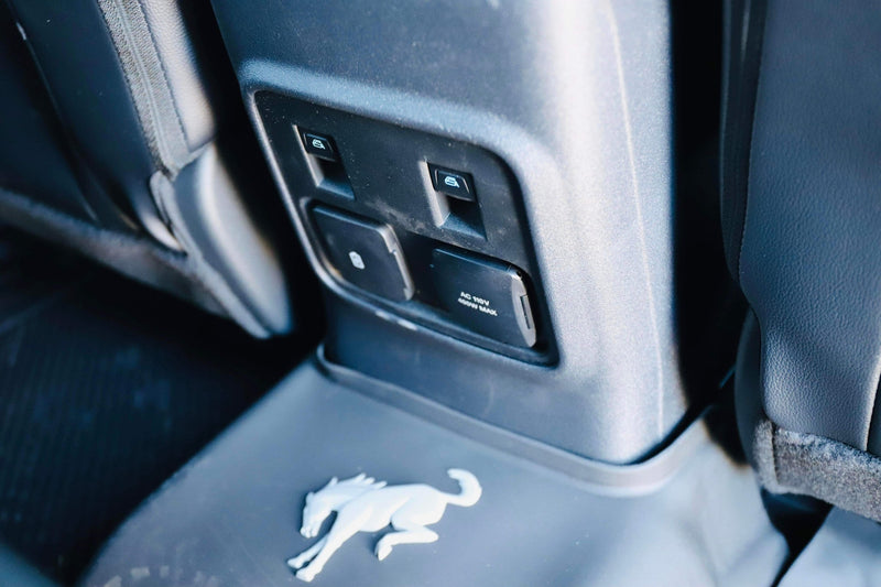 Back seat convenience in this RV rental: power window controls, AC 110V outlet for charging devices, and a cool Bronco logo. — photo 7