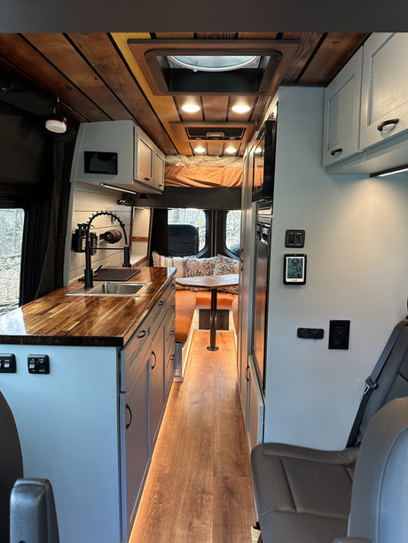 Step inside this stylish **RV rental**! Its custom wood and grey interior boasts a practical kitchen, cozy dining, and elevated bed.