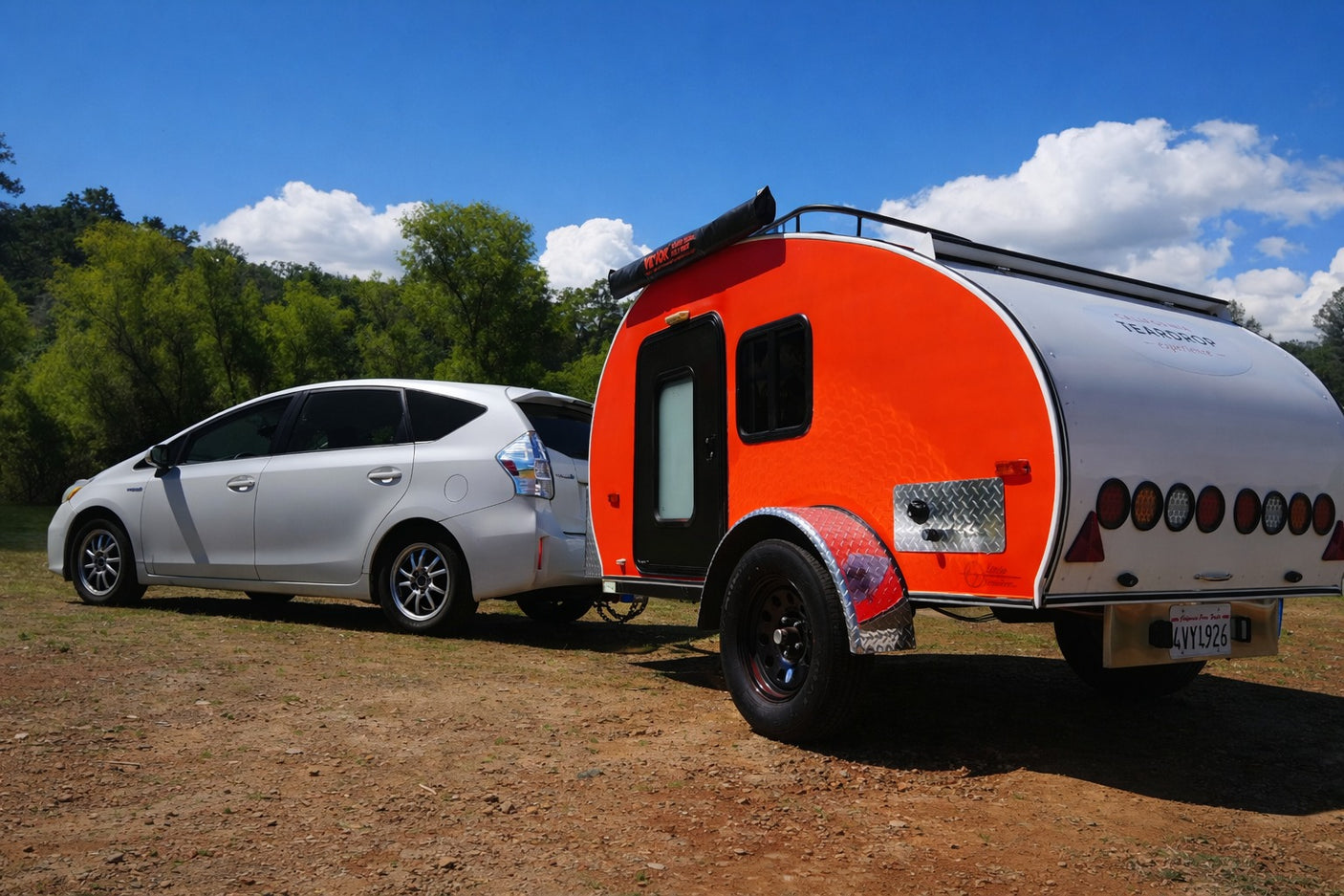 White Toyota Prius towing a bright orange teardrop RV rental, ready for adventure outdoors.