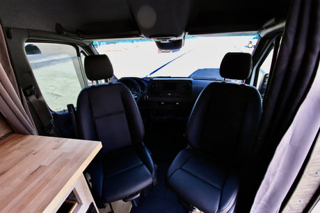 Spacious RV rental interior: front seats, dashboard, and a wood countertop inside this camper van, ready for adventure.