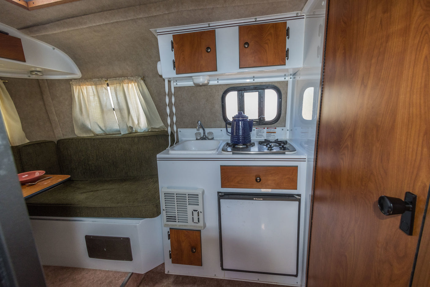 Compact kitchen and dinette inside an RV rental, featuring a sink, stove, fridge, and overhead storage.