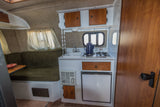 Compact kitchen and dinette inside an RV rental, featuring a sink, stove, fridge, and overhead storage.