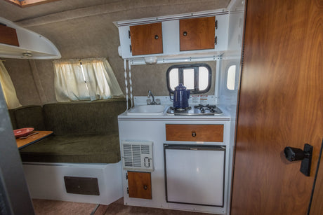 Compact kitchen and dinette inside an RV rental, featuring a sink, stove, fridge, and overhead storage.