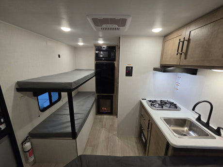Inside this rv rental: practical bunk beds, a compact kitchen with stove, sink, microwave, and mini-fridge, all in a modern setting.