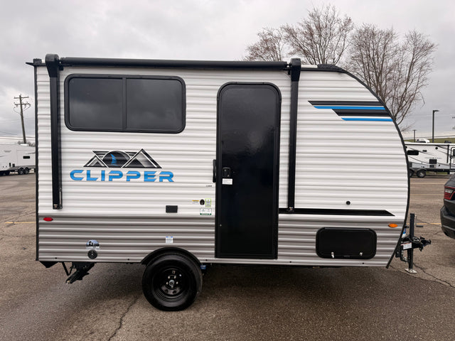 A white Clipper travel trailer, an ideal rv rental unit, parked on a gray day. Features black windows, door, and awning.