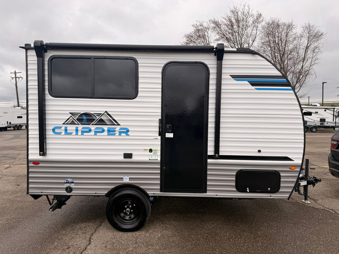 A white Clipper travel trailer, an ideal rv rental unit, parked on a gray day. Features black windows, door, and awning.