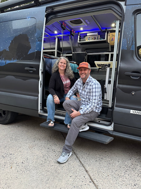 Smiling couple sits inside their customized camper van RV rental, showcasing its unique starry exterior and cozy blue-lit interior.