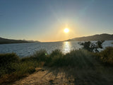 Beautiful sunset over a calm lake, with hills and foreground plants. Perfect scenic stop for your RV rental.