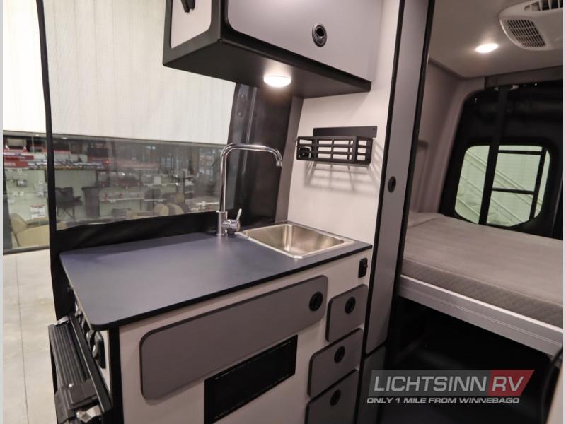 Explore this RV rental's compact interior: kitchen with sink, counter, storage, and a cozy sleeping area.
