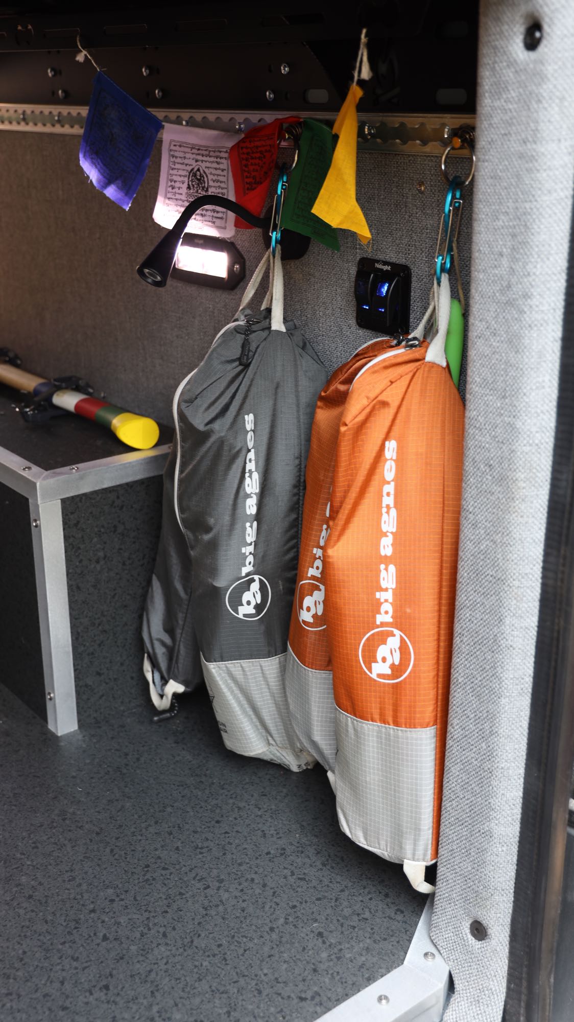 Inside an **rv rental**, Big Agnes bags hang near prayer flags and a light, showcasing organized storage for travel gear.