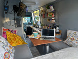 Cozy RV rental interior with a mobile office setup, laptop, kitchen area, TV, and vibrant pillows, perfect for van life.
