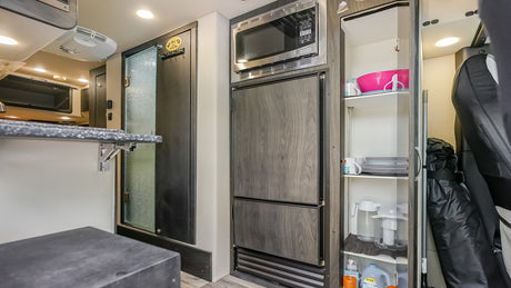 Experience this RV rental's clever interior: compact kitchen with microwave, fridge, pantry, and coat rack near the door.