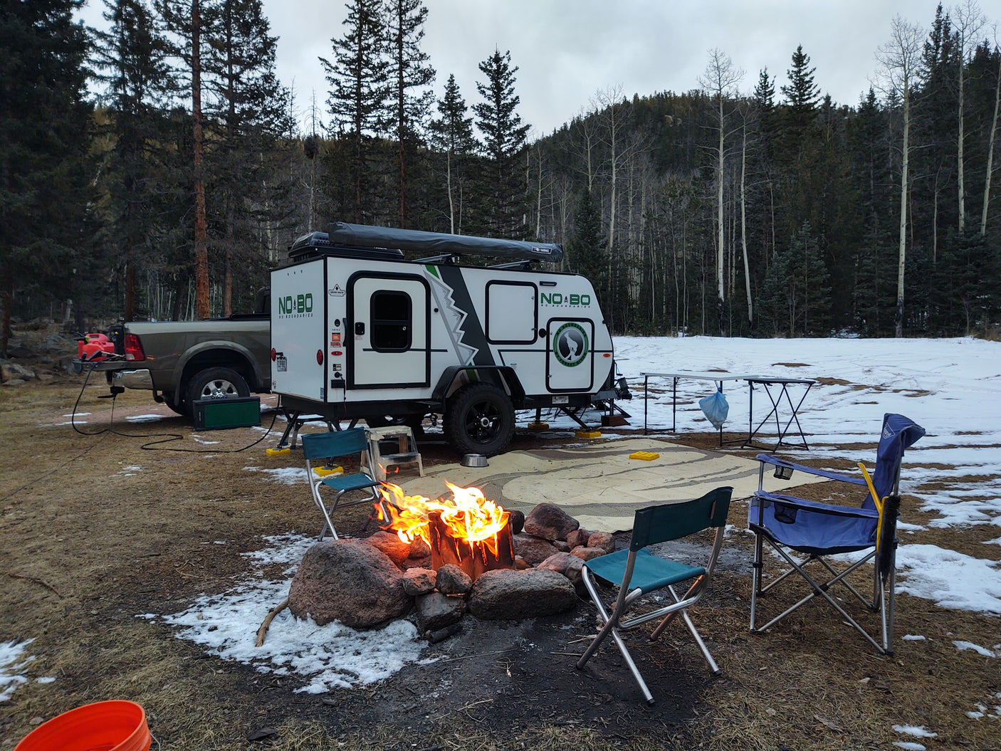 Cozy rv rental setup with a campfire and truck in a snowy forest. Perfect for winter camping trips!