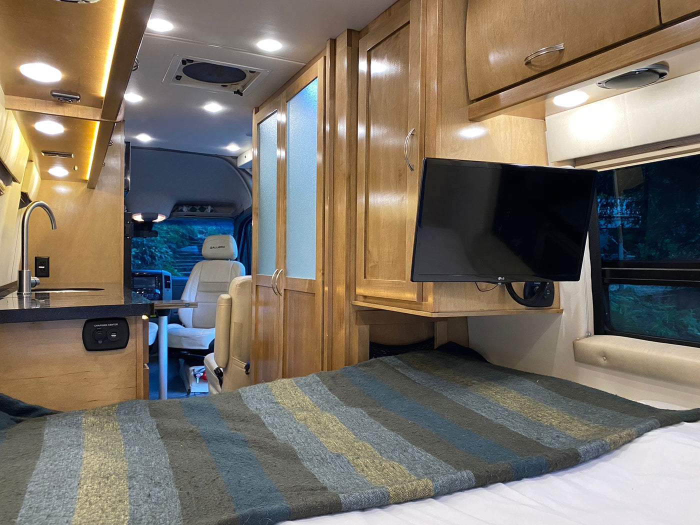  and cream leather swivel seats with a dining table.|An RV rental interior with a cozy bed — photo 4