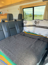Cozy RV rental interior: rear seating, bed with blankets & pillows, plus a scenic mountain view. Ideal for travel.