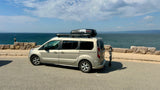 RV rental van with Yakima cargo box and bike rack, parked by the sea on a sunny day, ready for adventure trips.