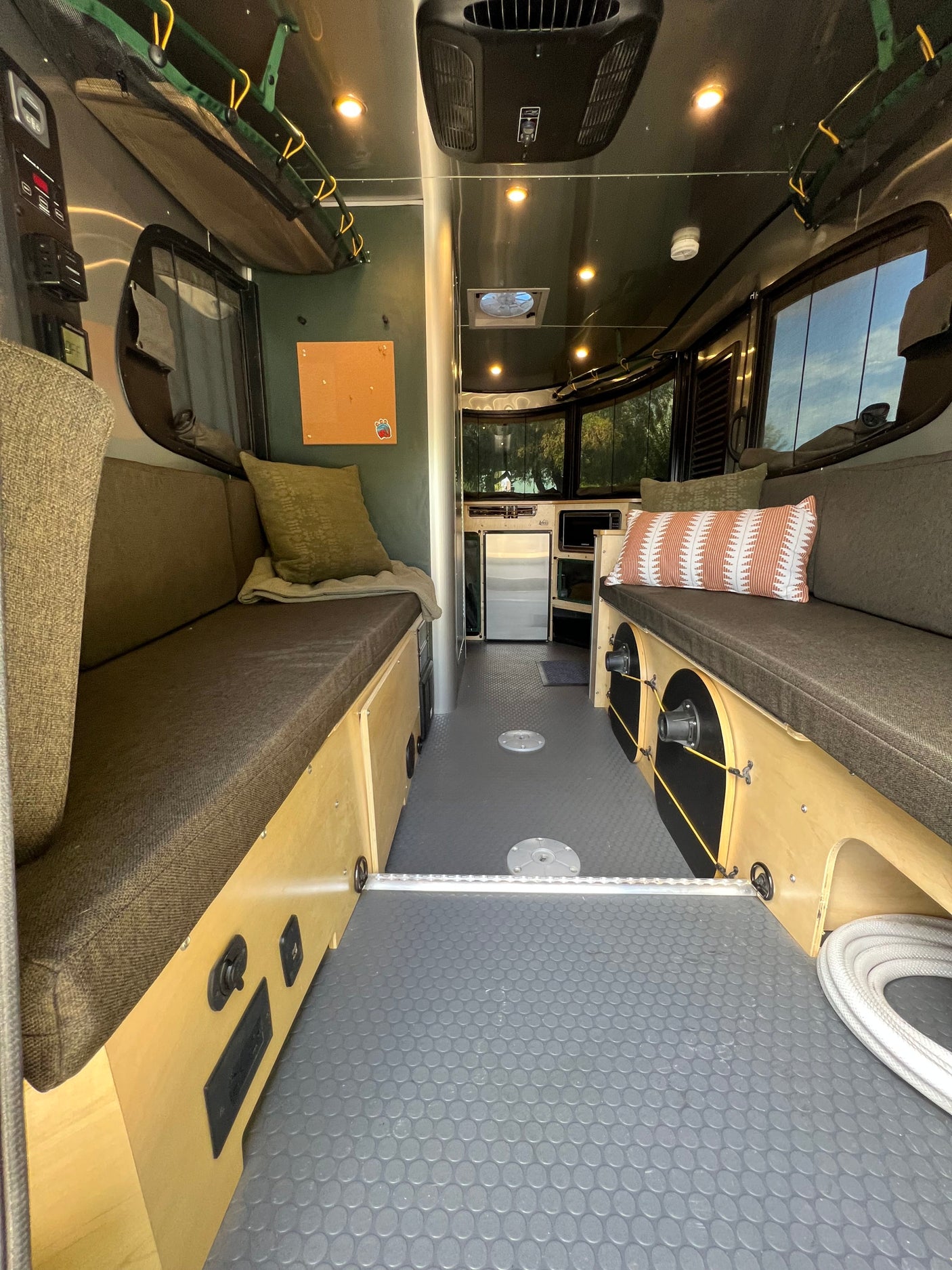 Interior view of an RV rental: features long benches, a mini-kitchen, and overhead storage for comfortable travel.