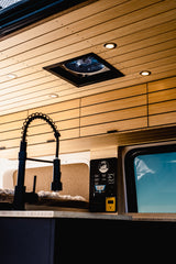 Modern RV rental interior featuring a stylish wooden slatted ceiling, a modern kitchen faucet, and a control panel for van systems.