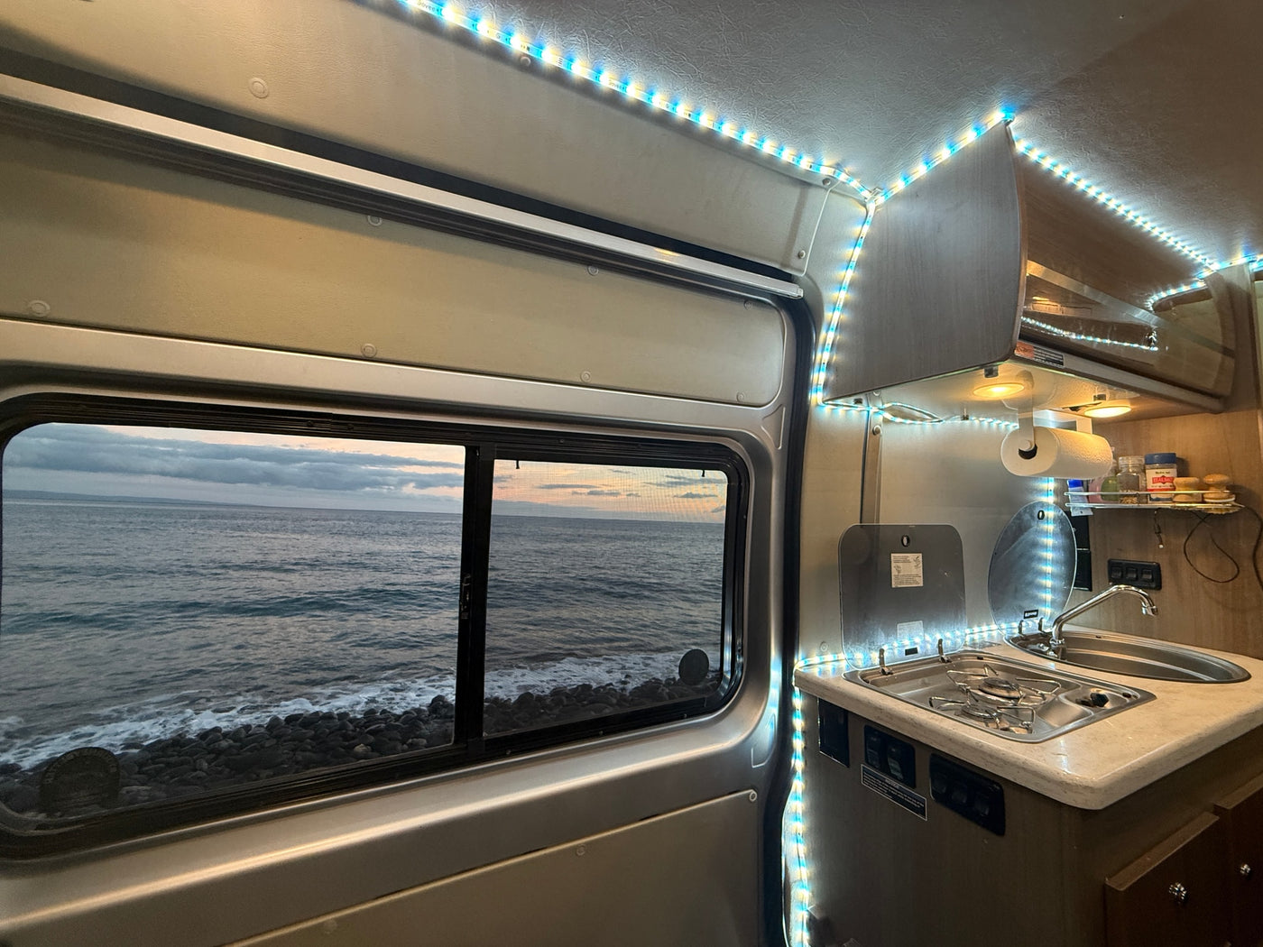 Inside an RV rental, showing the kitchen area and a scenic window view of the ocean & rocky shore. — photo 20