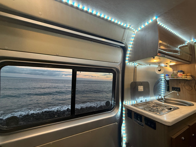 Inside an RV rental, showing the kitchen area and a scenic window view of the ocean & rocky shore. — photo 20