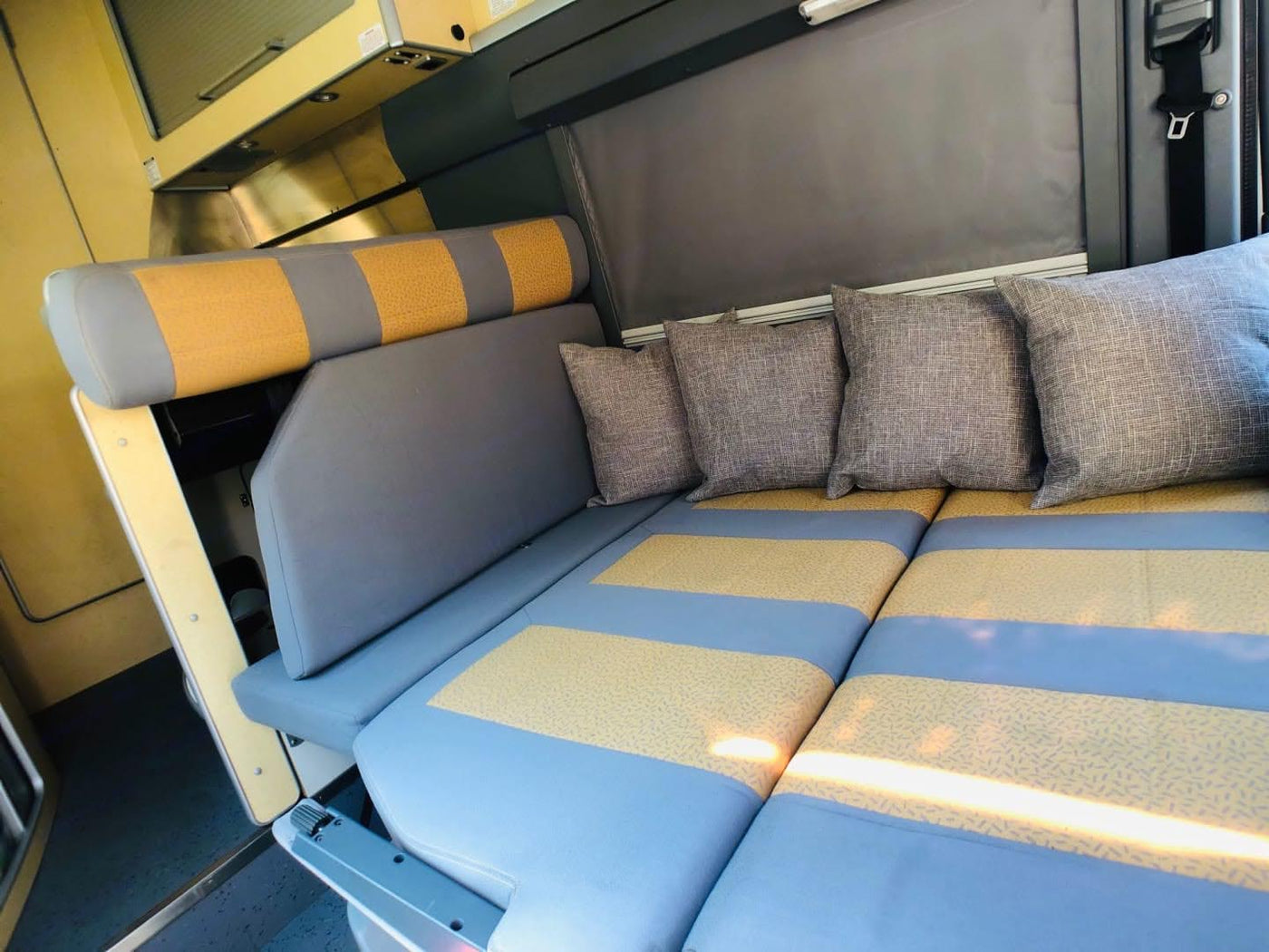 Cozy rv rental interior: comfortable seating and bed setup with gray & yellow striped cushions and throw pillows. — photo 15