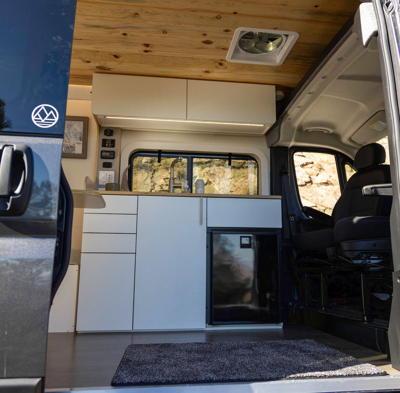 RV rental: Inside a modern camper van with a light wood ceiling, white cabinetry, kitchen, fridge, and control panel. — photo 3