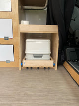 RV rental interior: a pull-out portable toilet hidden in custom wood cabinetry, offering discreet and compact bathroom solution.