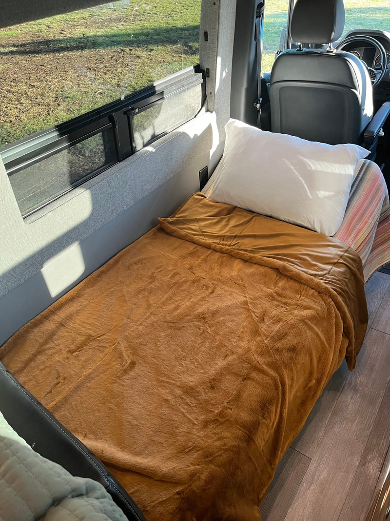 Cozy RV rental interior, featuring a comfy bed with a brown blanket and a bright window view of green grass. — photo 12