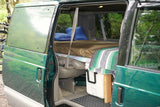Open side door of a green camper van revealing a bed, pillows, and cooler. An ideal RV rental for outdoor adventures.