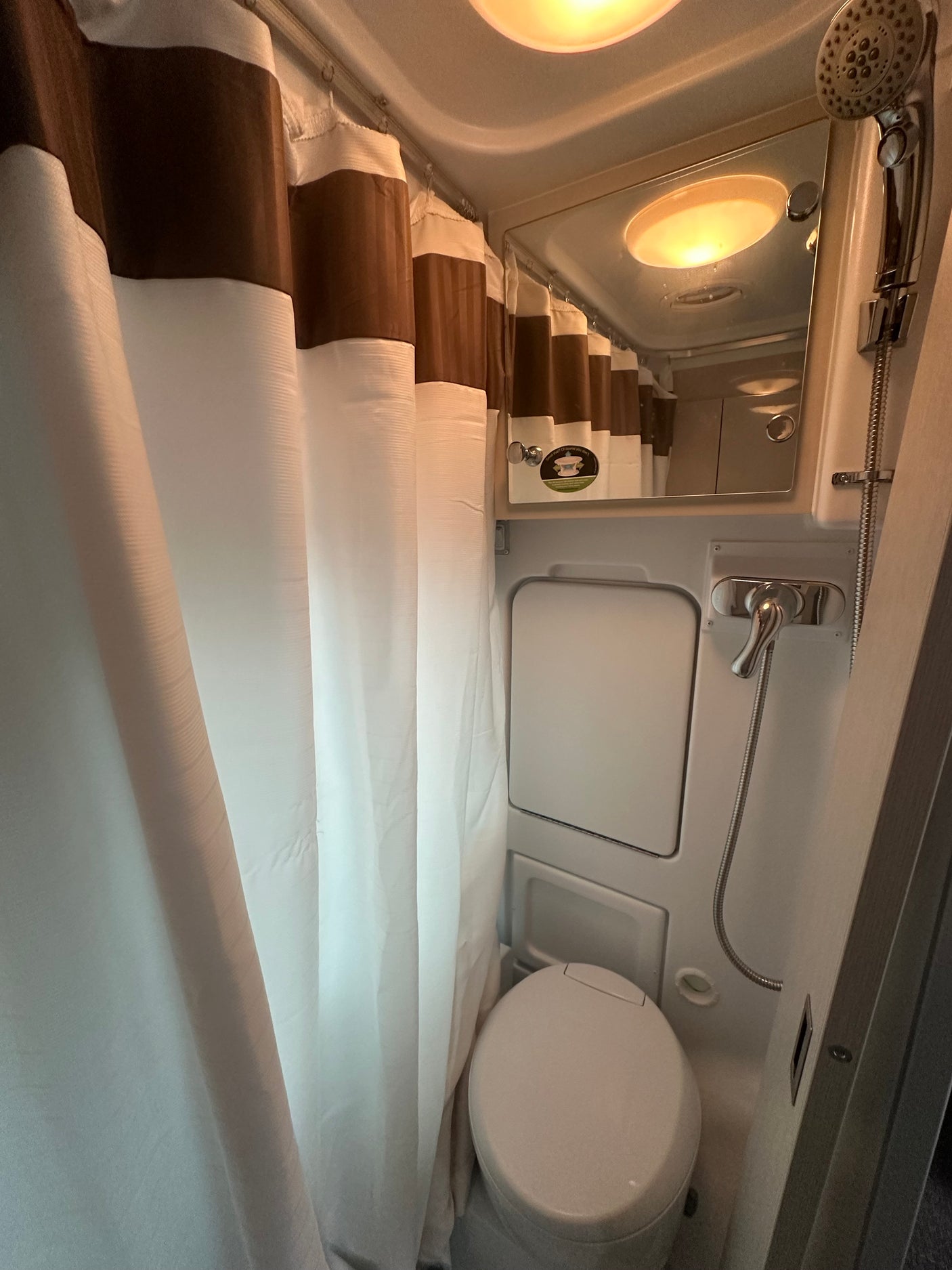 Compact RV rental wet bath featuring a toilet, shower, and curtain for convenient travel.