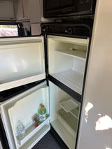 Open RV rental refrigerator with separate freezer, showing empty shelves and a few drinks in the door for your road trip.