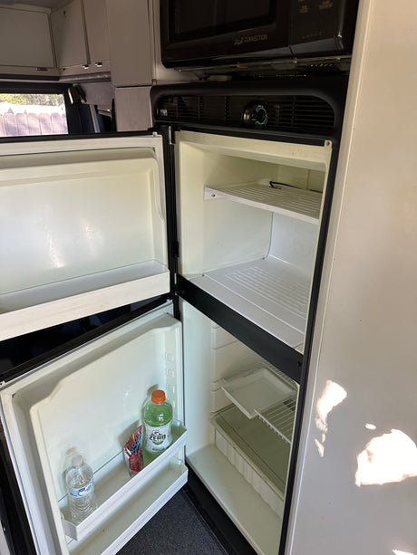 Open RV rental refrigerator with separate freezer, showing empty shelves and a few drinks in the door for your road trip.