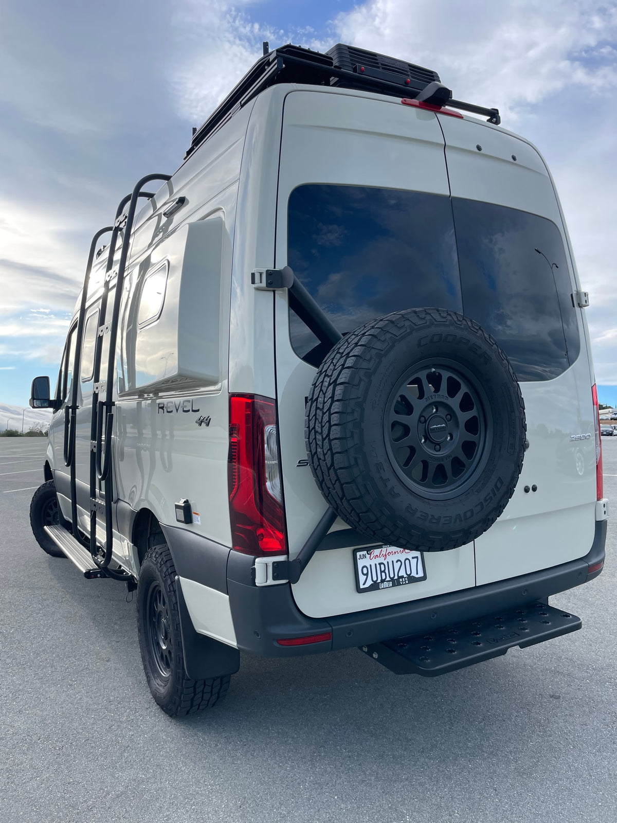 This white Winnebago Revel camper van, a great RV rental option, features a roof rack, ladder, and rear spare tire. — photo 4