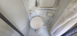 Inside an RV rental, showing a compact bathroom with a white toilet, shower fixtures, and curtain.