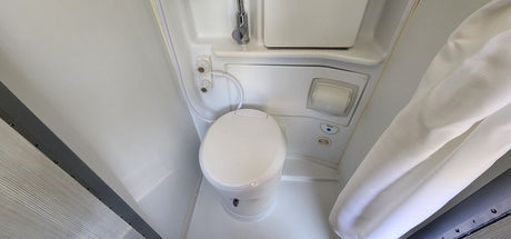 Inside an RV rental, showing a compact bathroom with a white toilet, shower fixtures, and curtain.