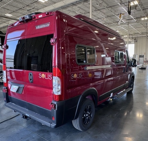  showcasing its exterior from the rear and side. Ready for adventure.|This deep red Winnebago Solis camper van — photo 1
